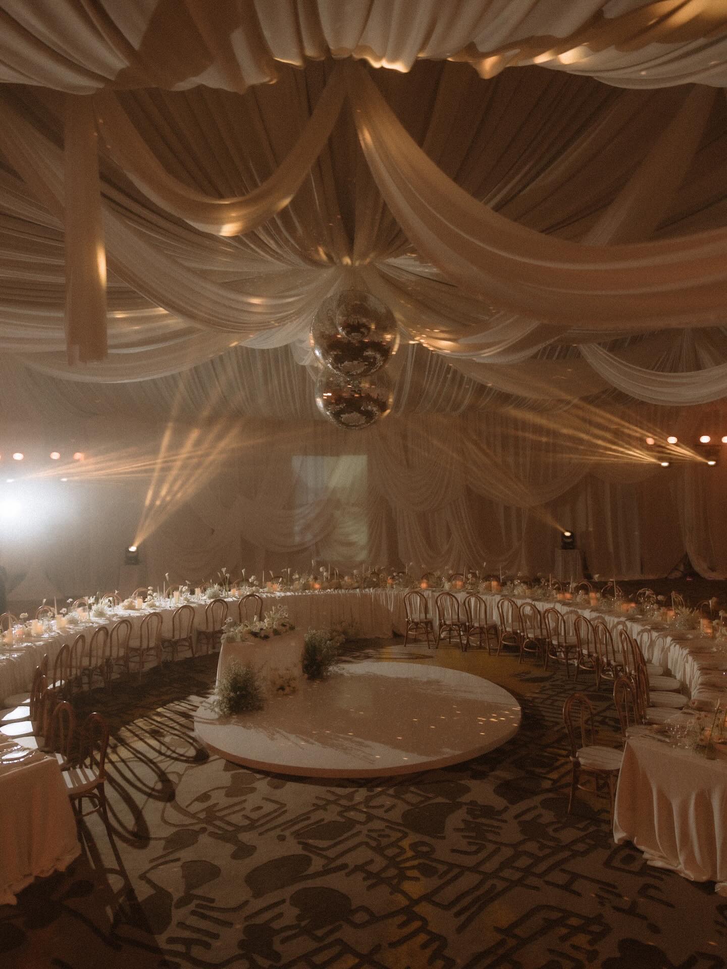 Indoor wedding reception with draped ceiling, warm lighting, and disco ball
