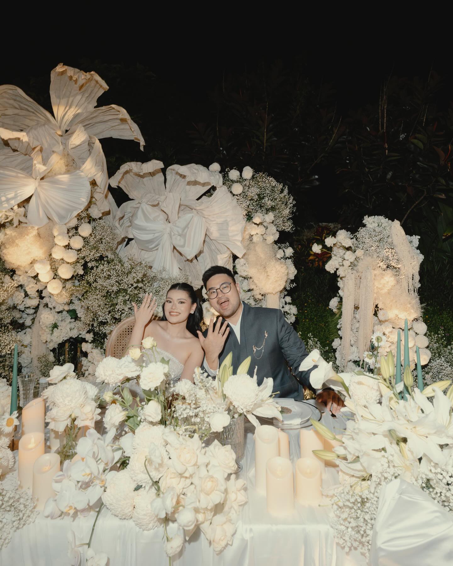 Wedding couple at a white floral reception table with candles